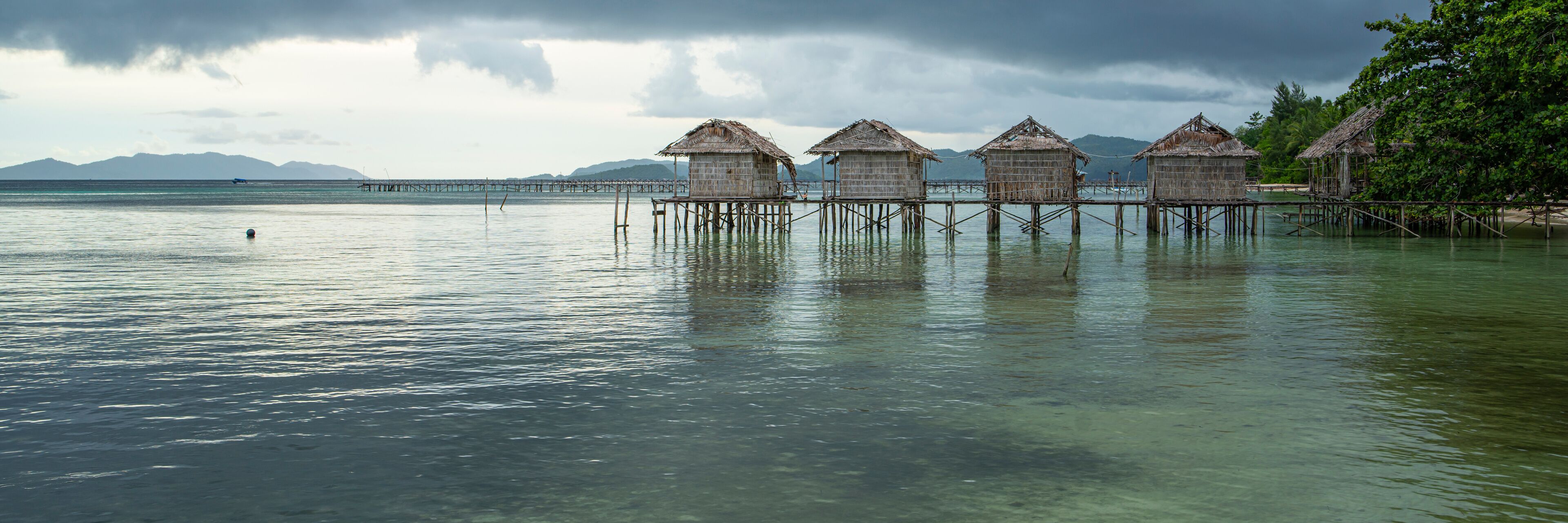 Overwater bungalows on stilts in a calm sea with a cloudy sky.