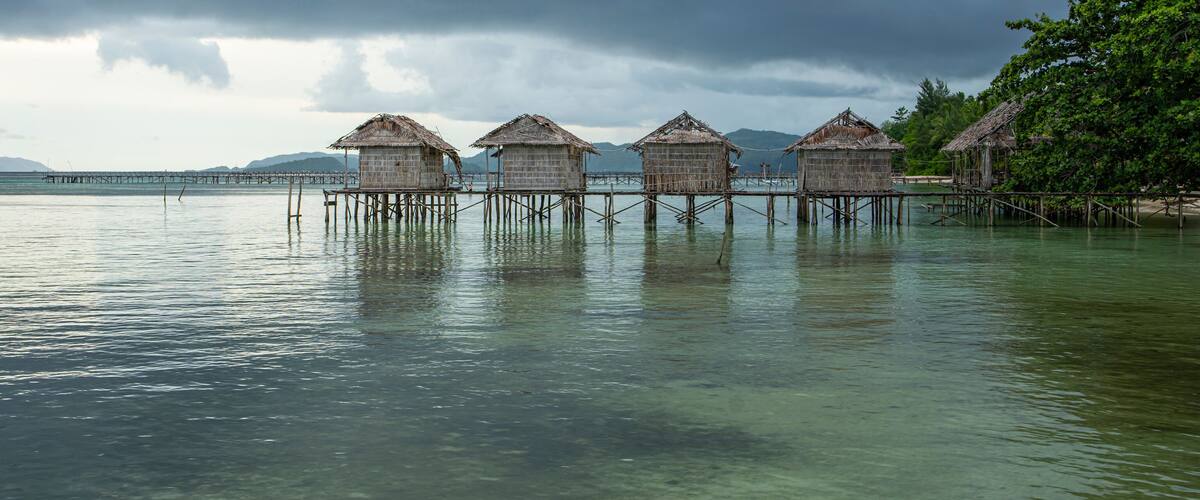 Overwater bungalows on stilts in a calm sea with a cloudy sky.
