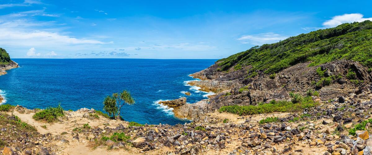 A coastal landscape with rocky terrain and dense greenery on hillsides.