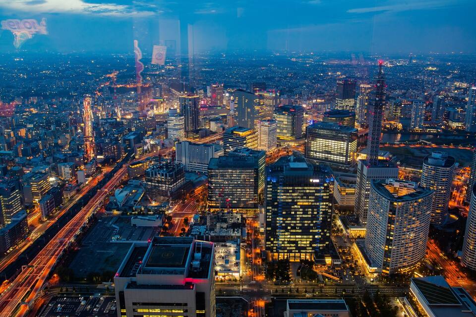 A cityscape at dusk with illuminated buildings and a river in the background.