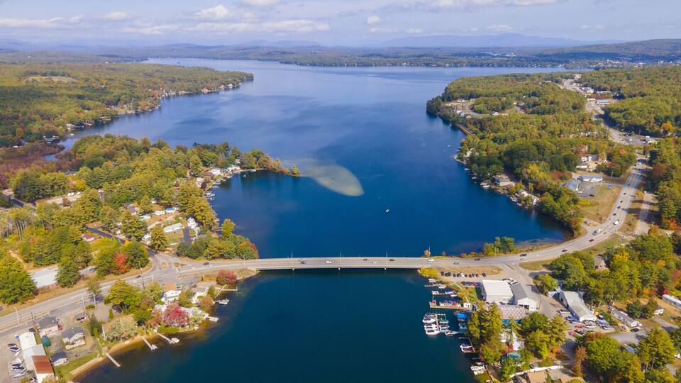 An aerial view of a lake surrounded by dense forests and a small town with a bridge connecting two sides.
