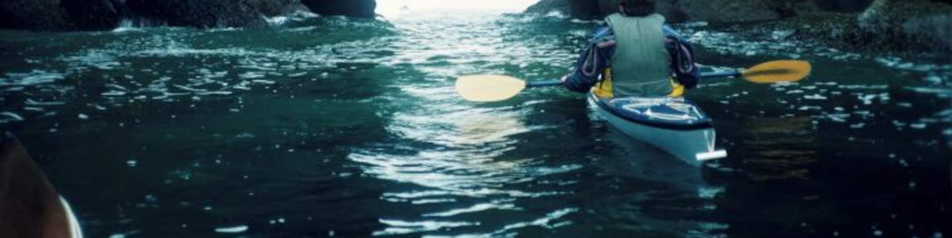 Kayaker approaching rock arch, Point of Arches, Washington, USA coast, rear view