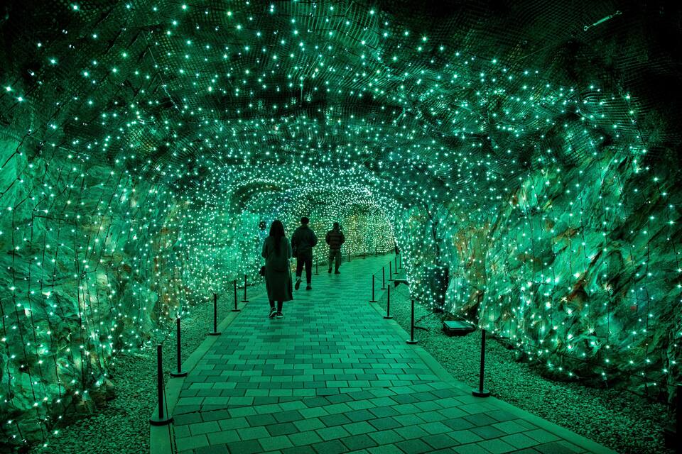 A tunnel with green lights and people walking through it.