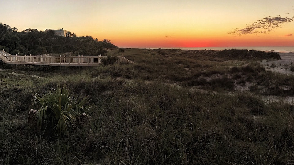 A sunset over a beach with a wooden boardwalk and dunes.
