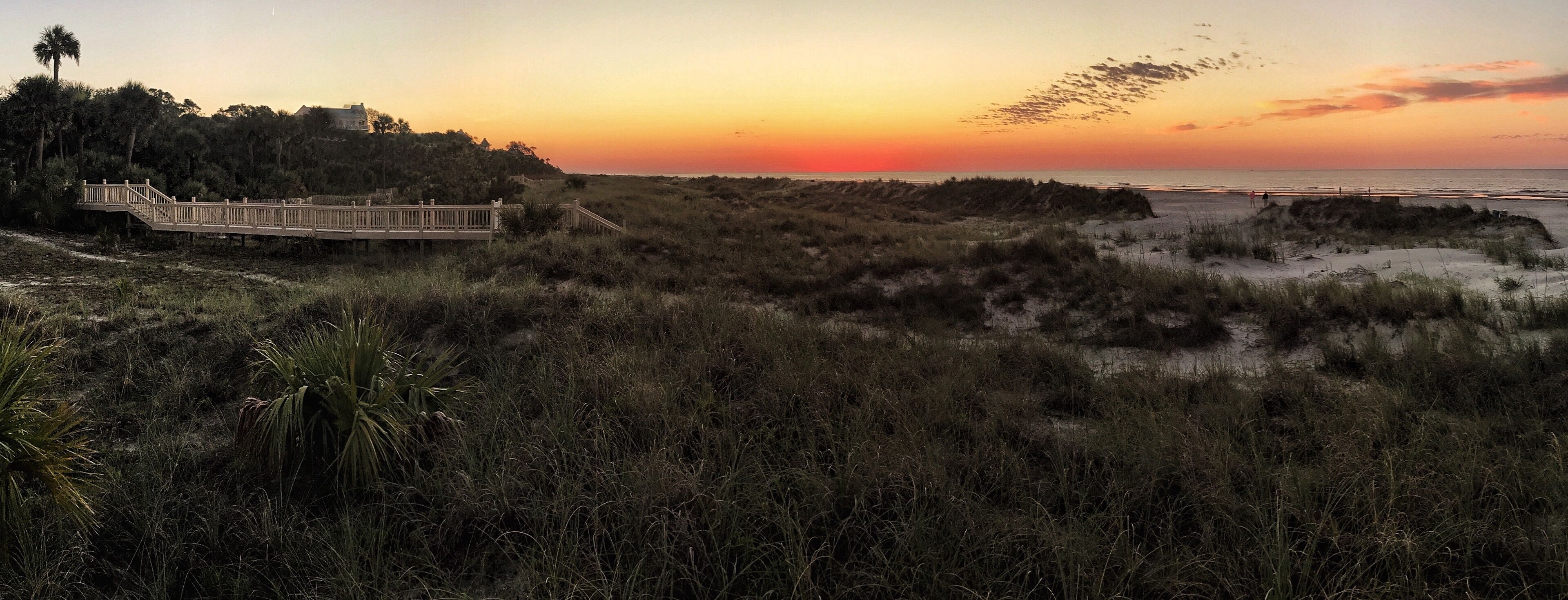 A sunset over a beach with a wooden boardwalk and dunes.