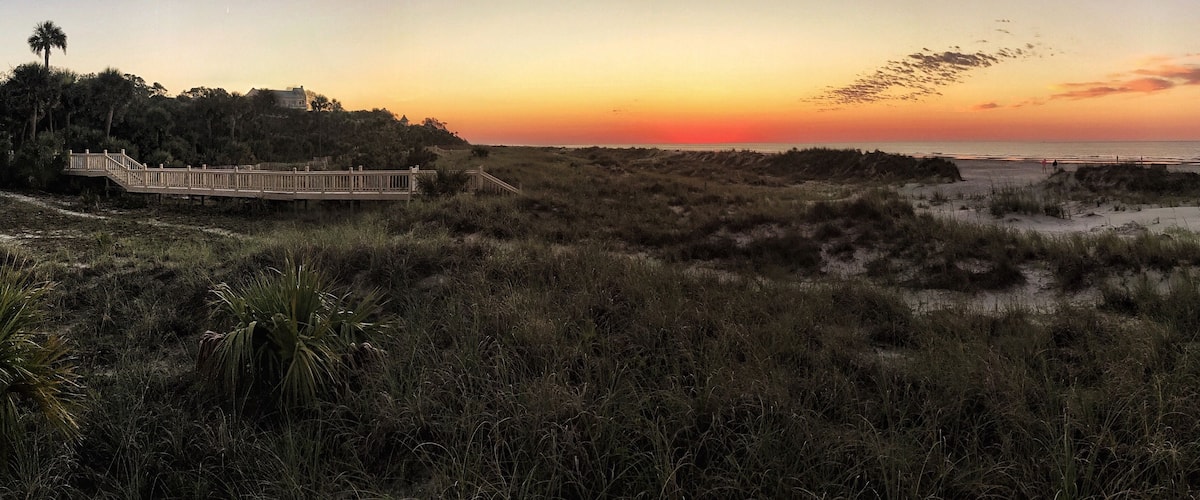 A sunset over a beach with a wooden boardwalk and dunes.
