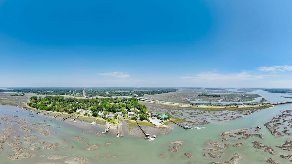 An aerial view of a coastal area with a pier extending into a lagoon, surrounded by scattered islands and a distant bridge.