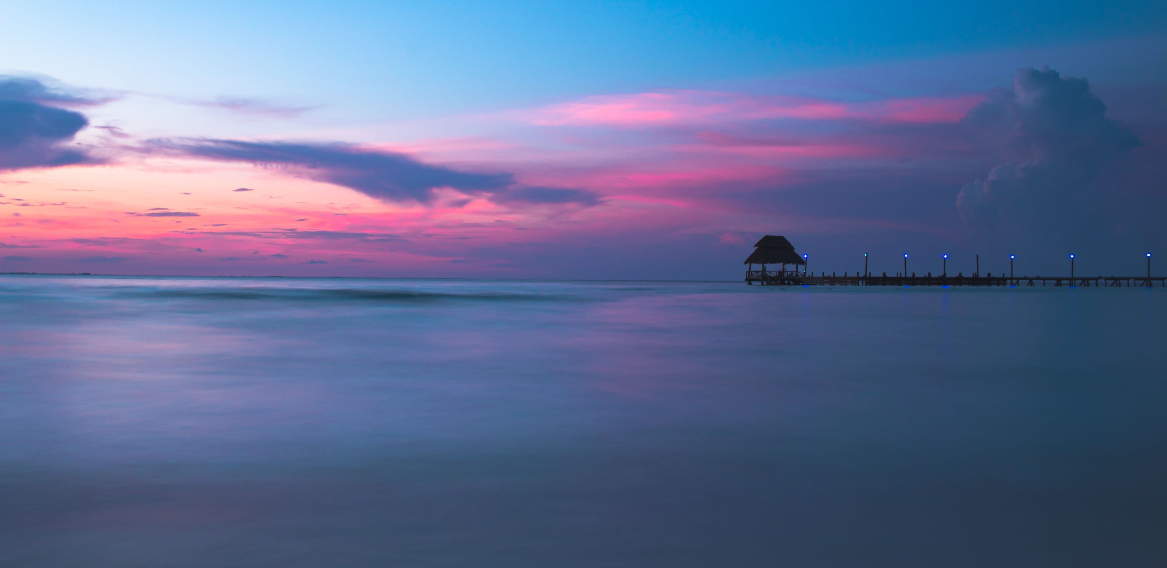 Isla Mujeres sunset on the beach with a small wooden cottage at the end of a pier in Mexico.