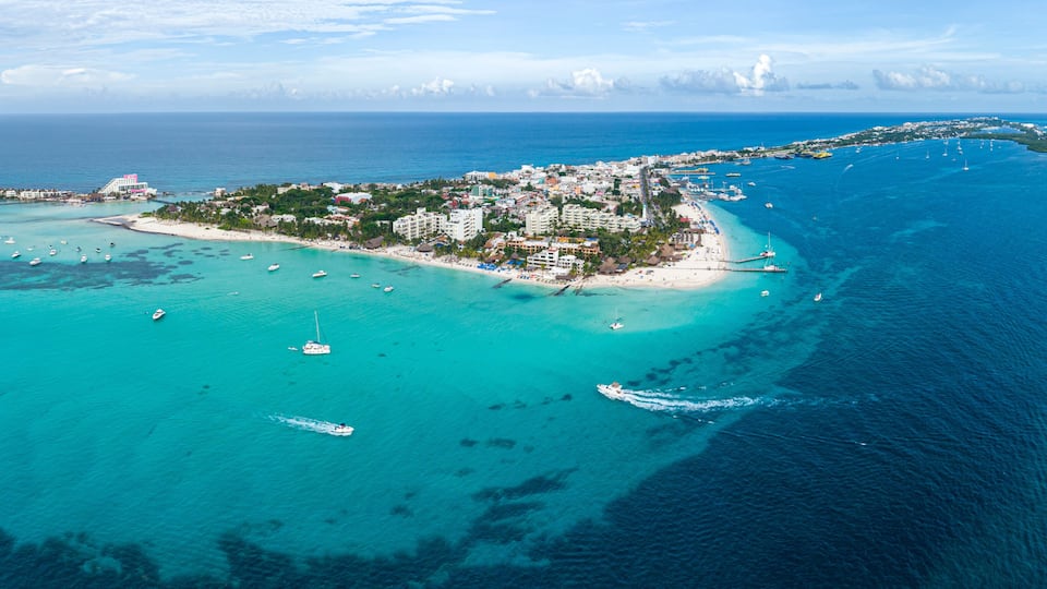 An aerial view of a coastal town with a beach, boats, and clear blue waters.