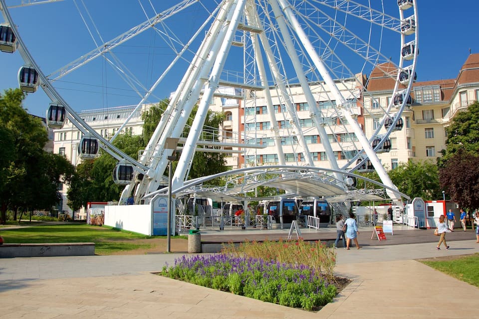 A Ferris wheel, a park with benches, and a building with a red roof.