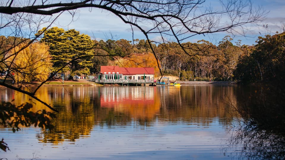 A lake with a house reflecting on the water, surrounded by trees and a clear sky.