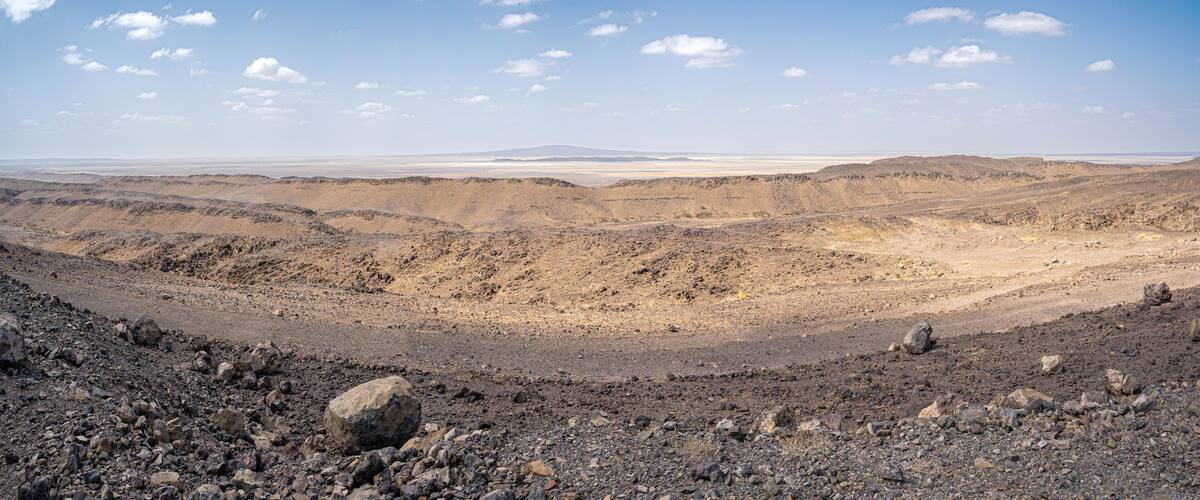 A barren desert landscape with rocky terrain and distant mountains.