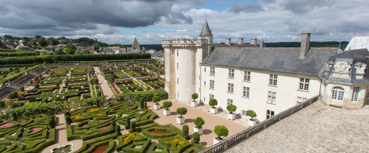 A historic castle with a formal garden, a large white building, and a stone wall.