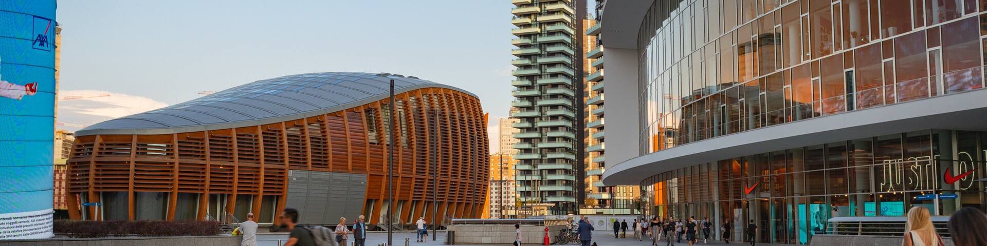 A modern urban plaza with a curved building, a tall residential tower, and a glass-fronted commercial building.