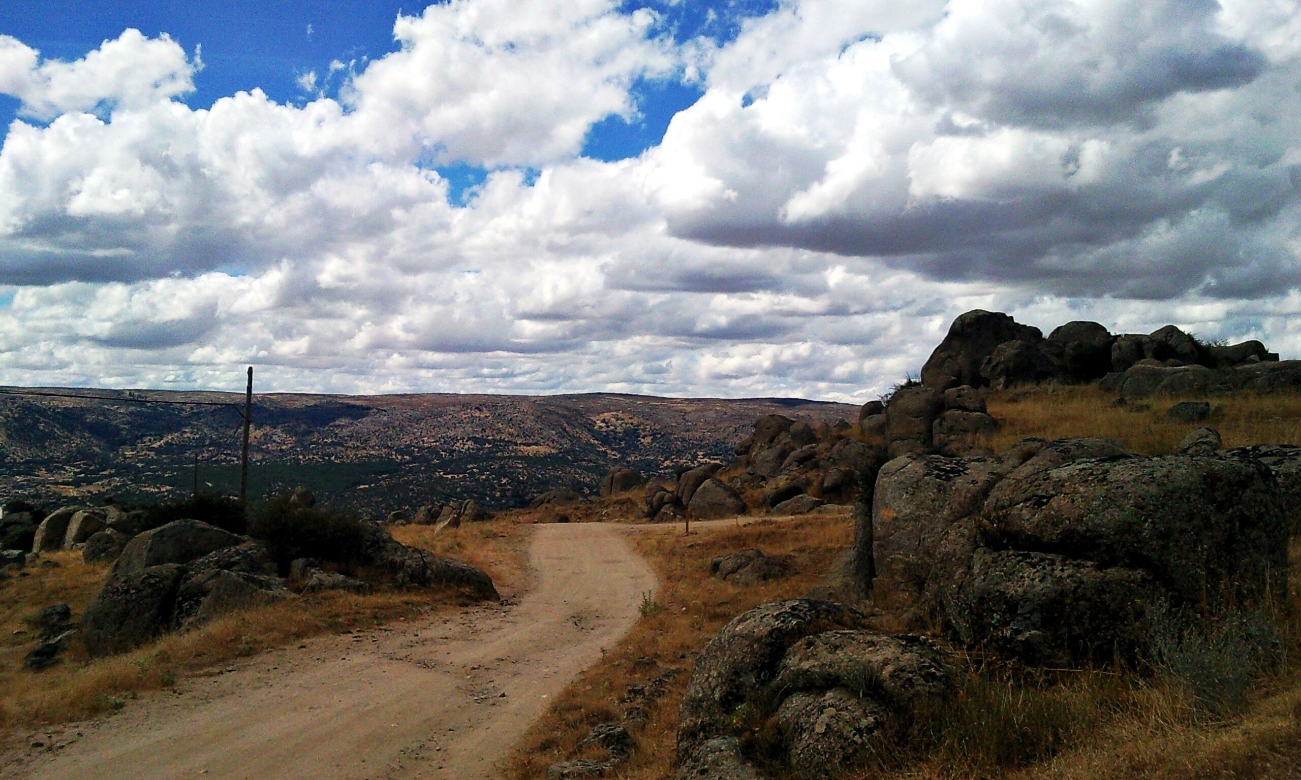 A dirt road winding through rocky terrain with a mountainous landscape in the background.