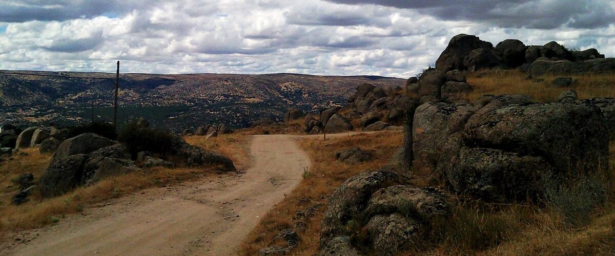 A dirt road winding through rocky terrain with a mountainous landscape in the background.