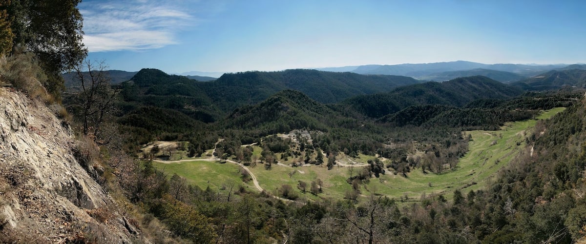 A mountainous landscape with a valley, forested areas, and a clear sky.
