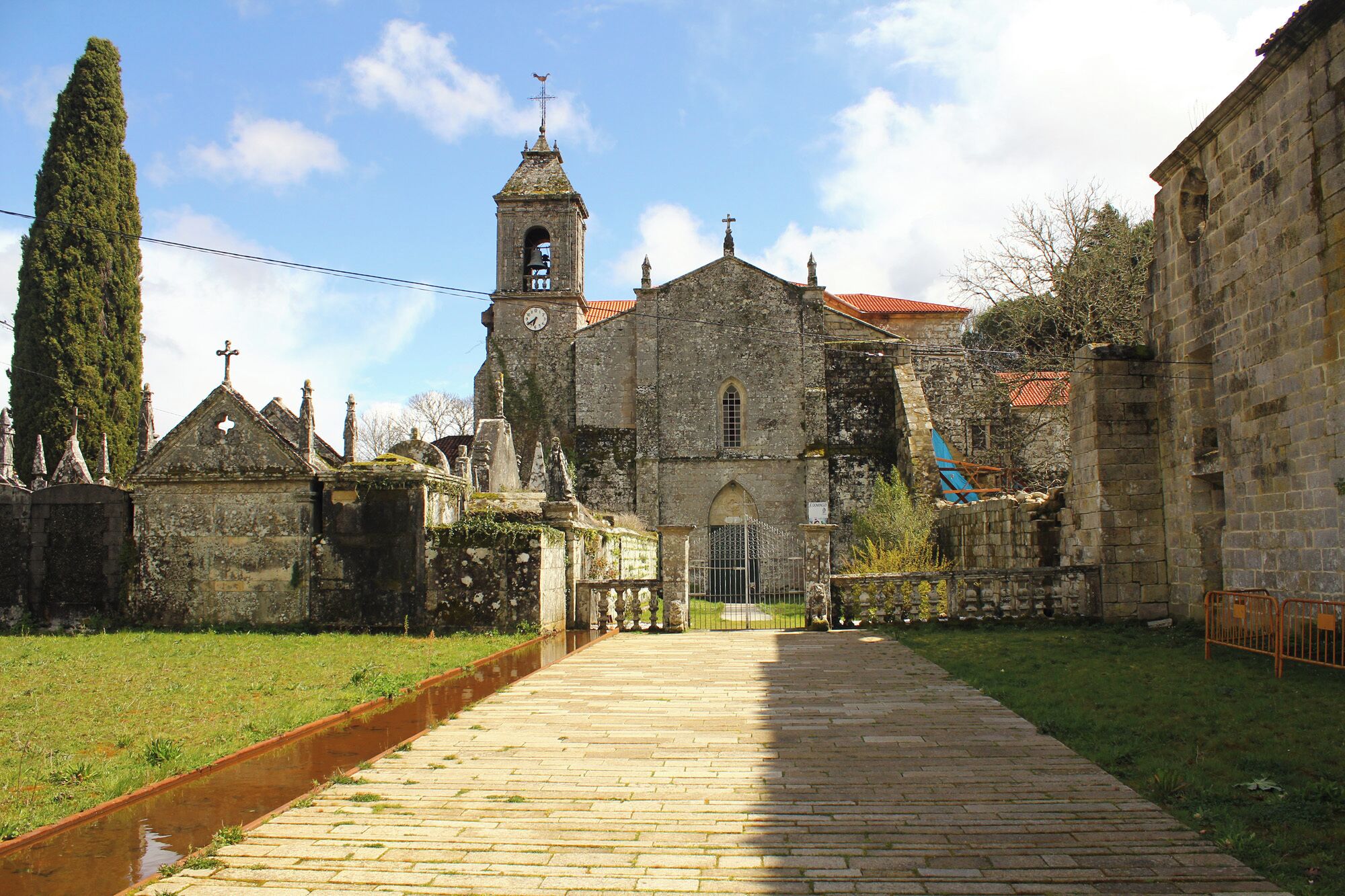 Una iglesia histórica con un campanario, rodeada de edificios de piedra y un estrecho sendero.