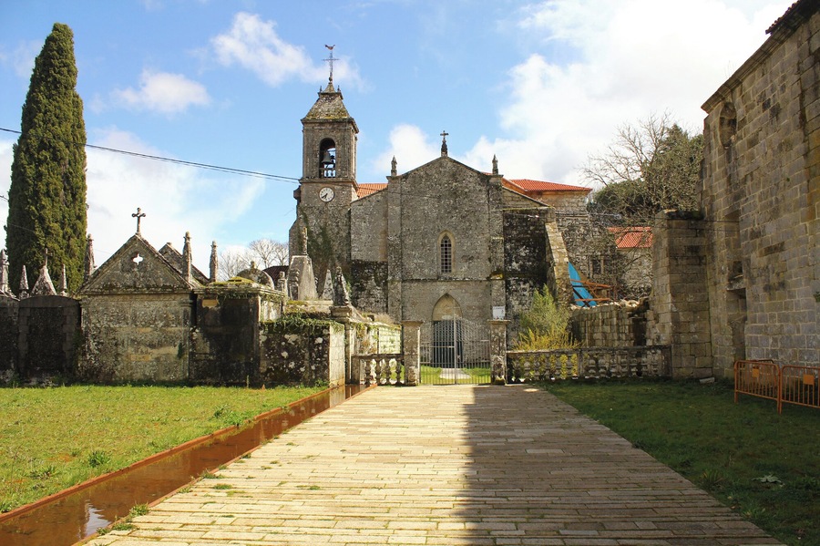 A historic church with a bell tower, surrounded by stone buildings and a narrow pathway.