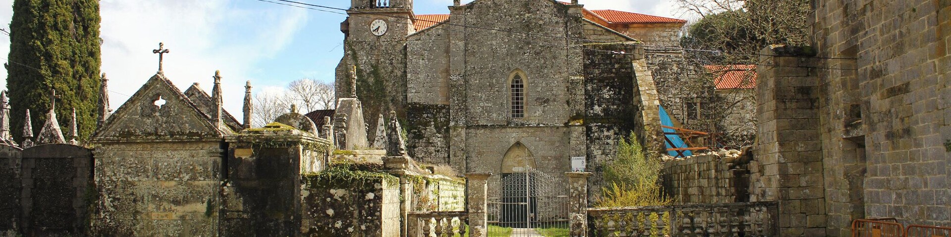 Una iglesia histórica con un campanario, rodeada de edificios de piedra y un estrecho sendero.