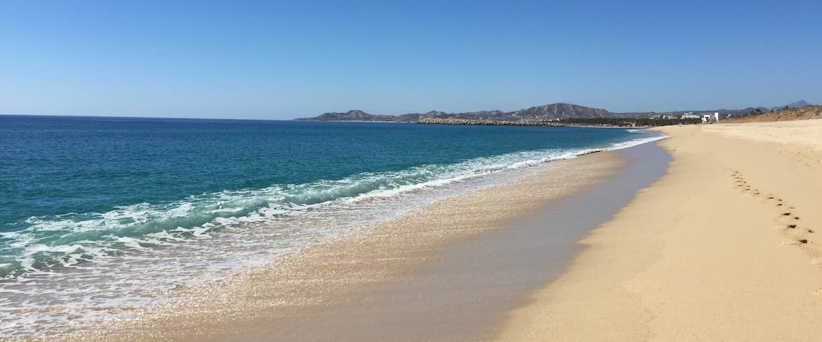 A sandy beach with gentle waves, a clear sky, and distant mountains.