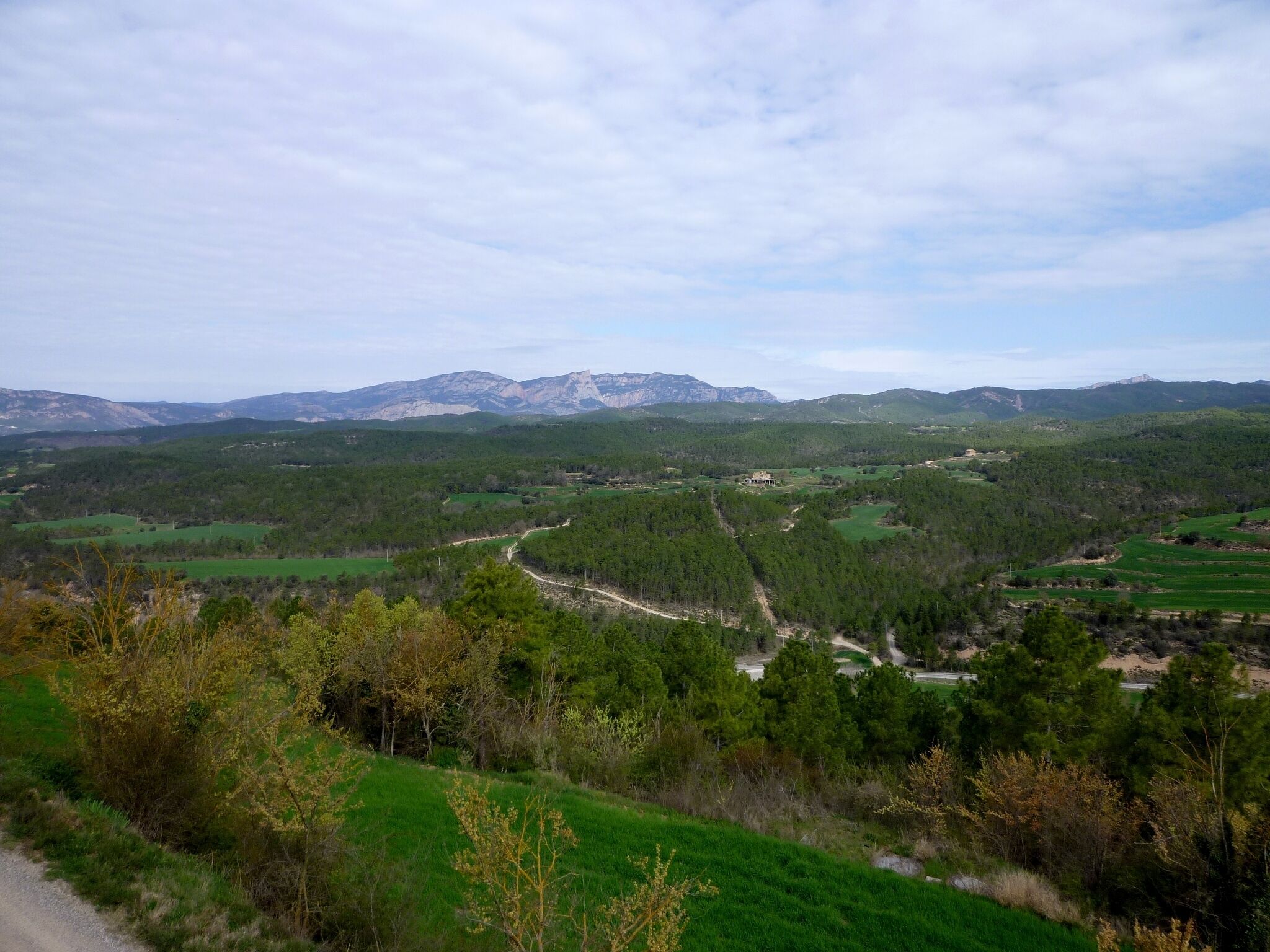 A mountainous landscape with a winding road, green fields, and scattered buildings.