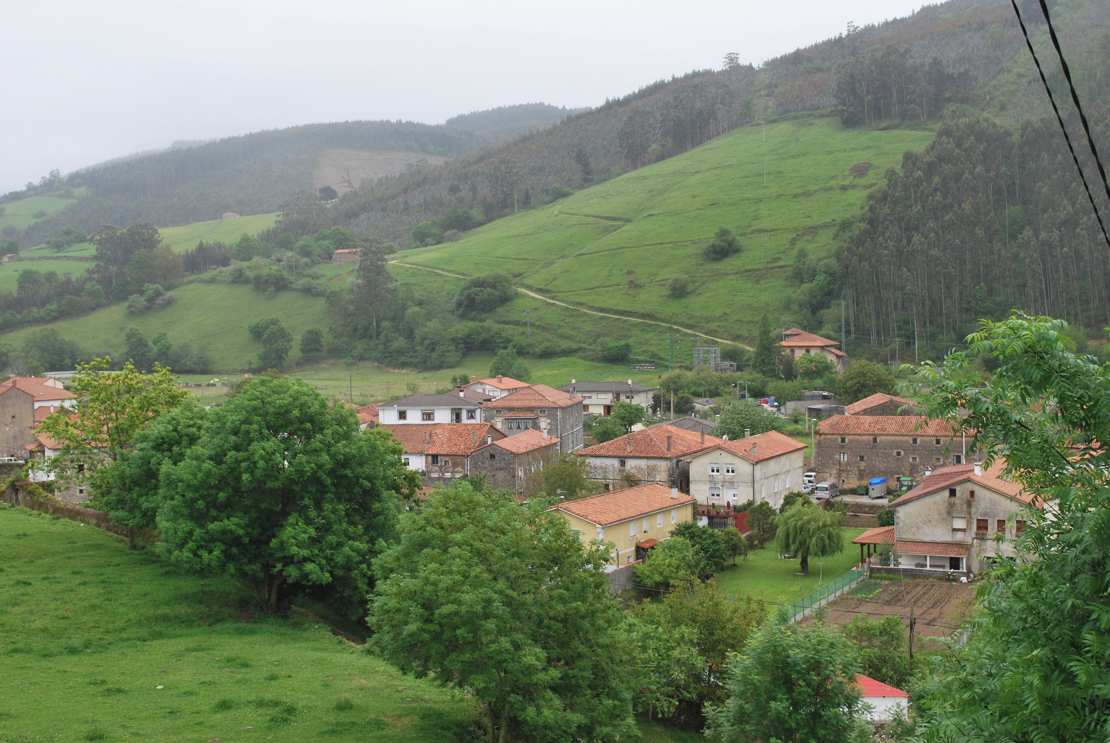 A rural village with terraced fields, traditional houses, and a hilly landscape.