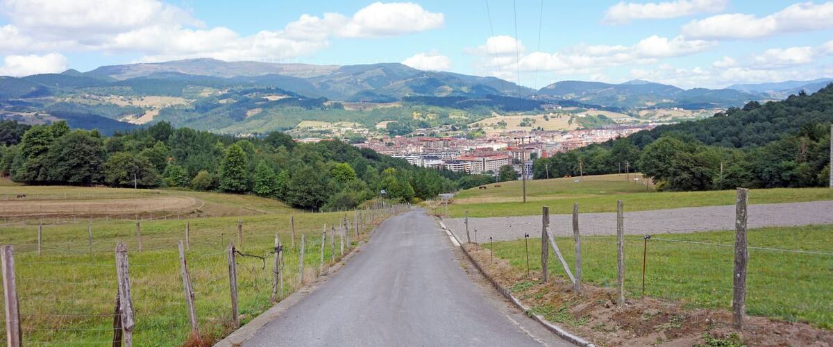 A rural road leading to a town surrounded by hills and greenery.