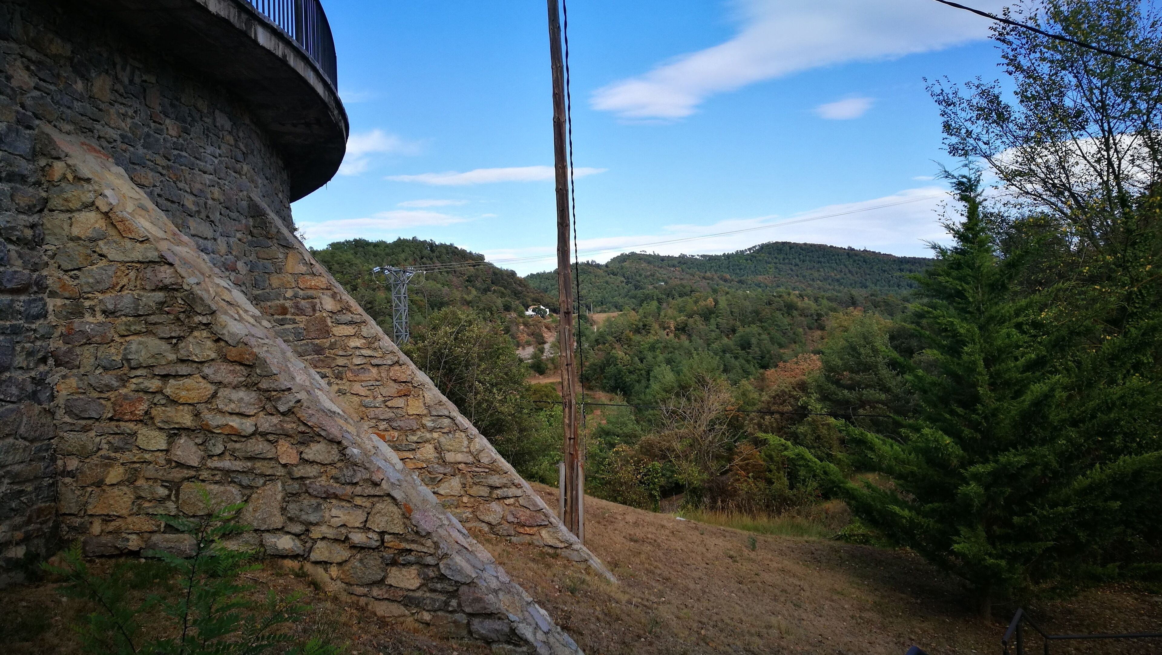 A stone wall, a wooden utility pole, and a forested hillside.