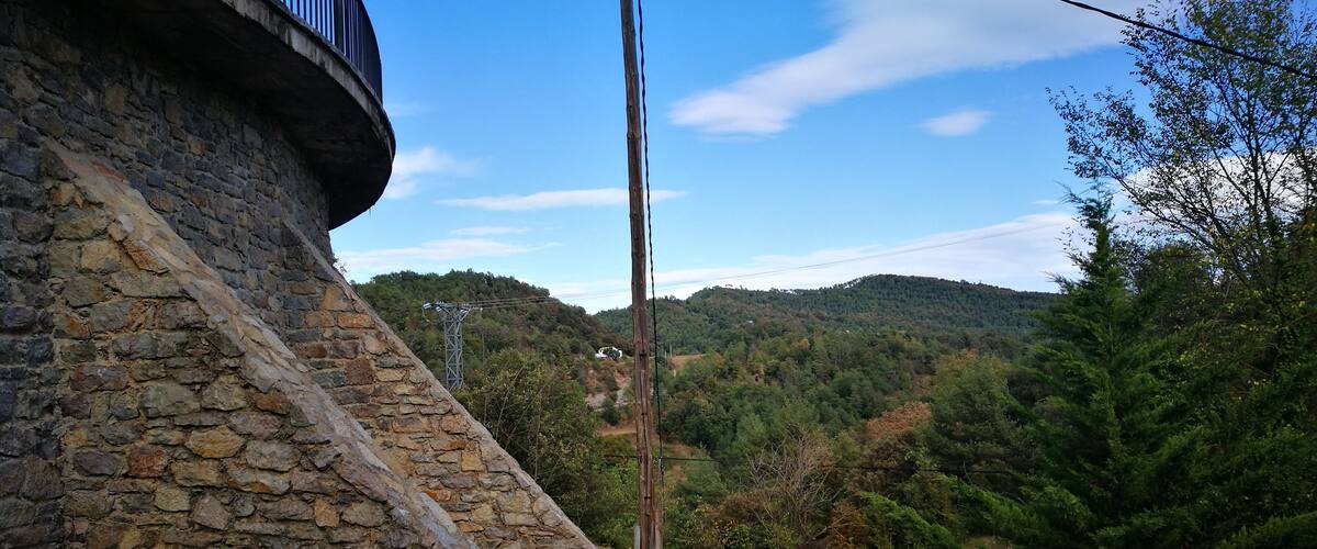 A stone wall, a wooden utility pole, and a forested hillside.