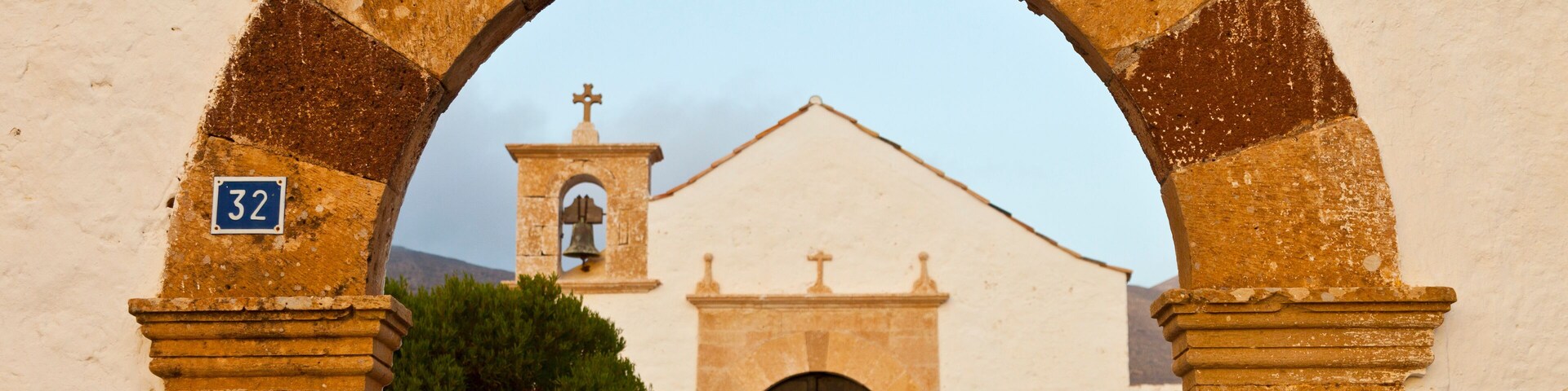 Un arco de entrada que conduce a una iglesia con un campanario y una cruz.