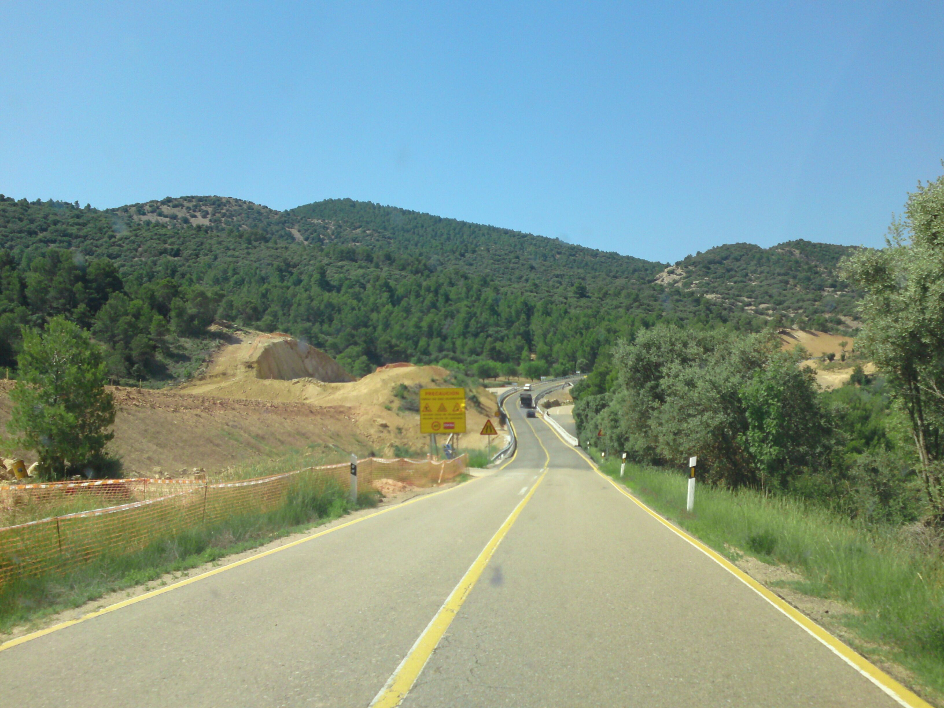 A two-lane road winding through a hilly landscape with dense forests and a clear sky.