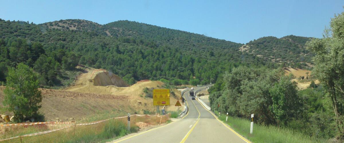 A two-lane road winding through a hilly landscape with dense forests and a clear sky.