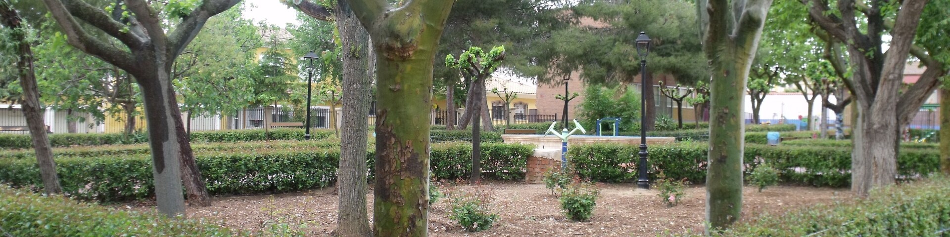 A park with trees, a metal fence, and a paved walkway.