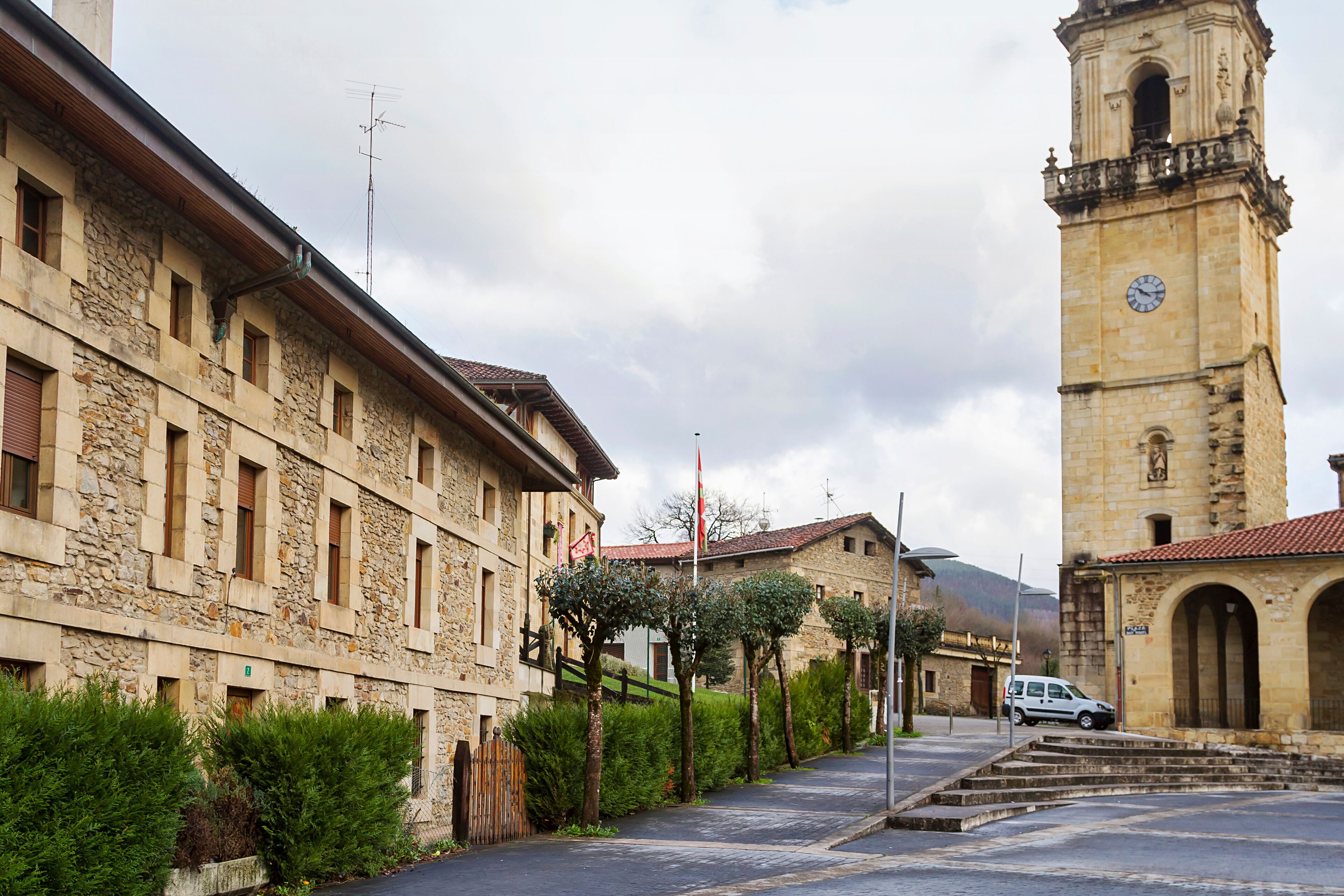A stone building with a clock tower, a paved street, and a parked car.