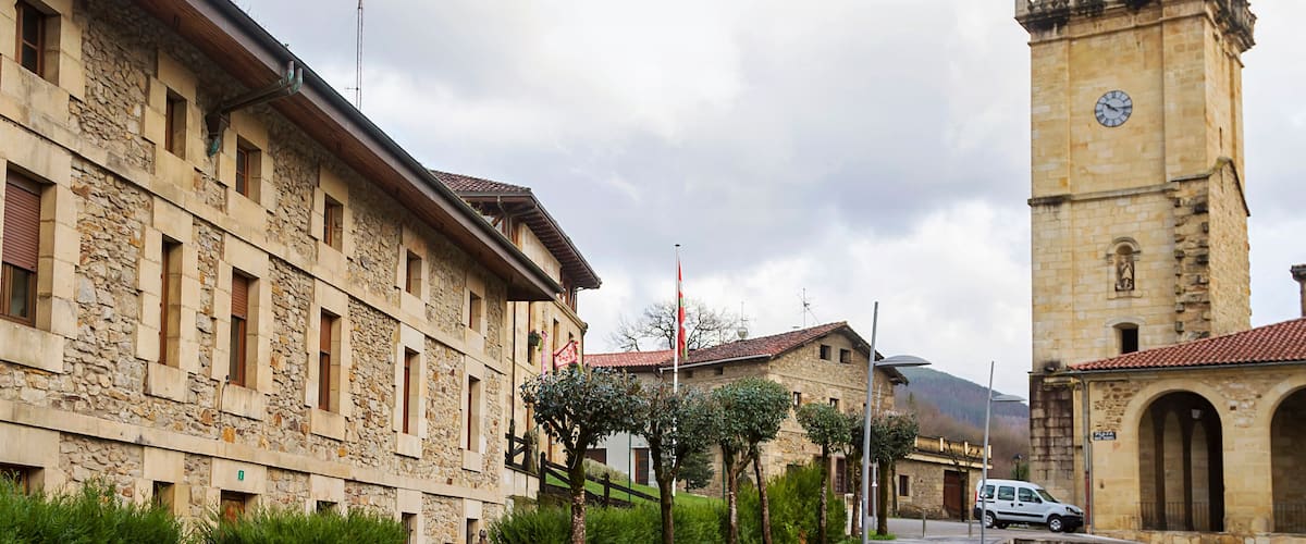A stone building with a clock tower, a paved street, and a parked car.