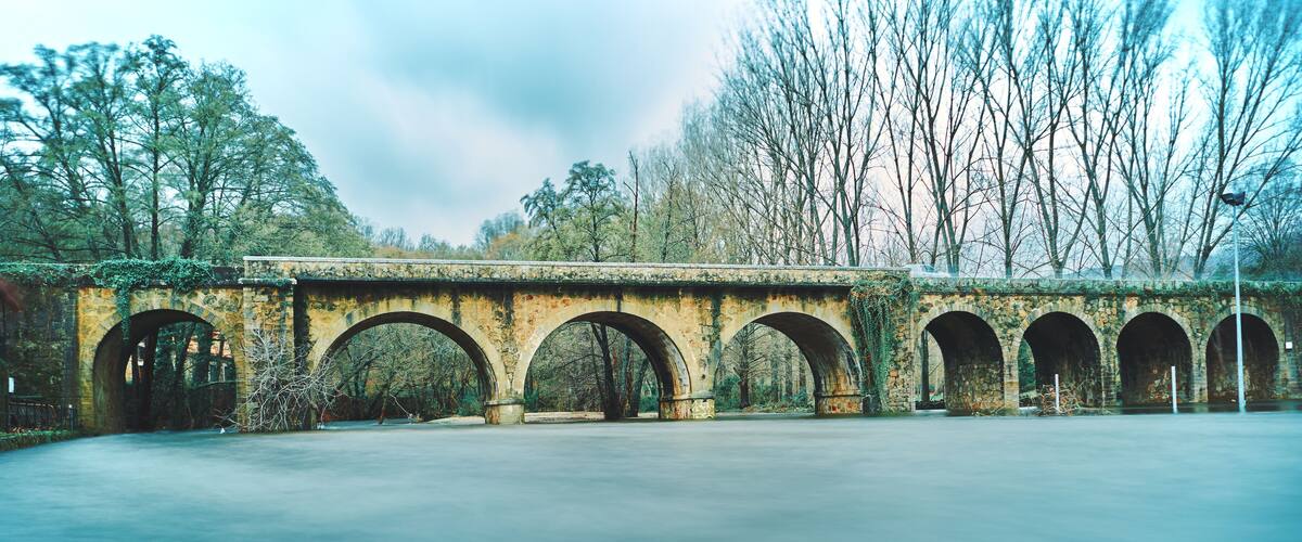 A stone bridge with multiple arches over a body of water, surrounded by trees and greenery.