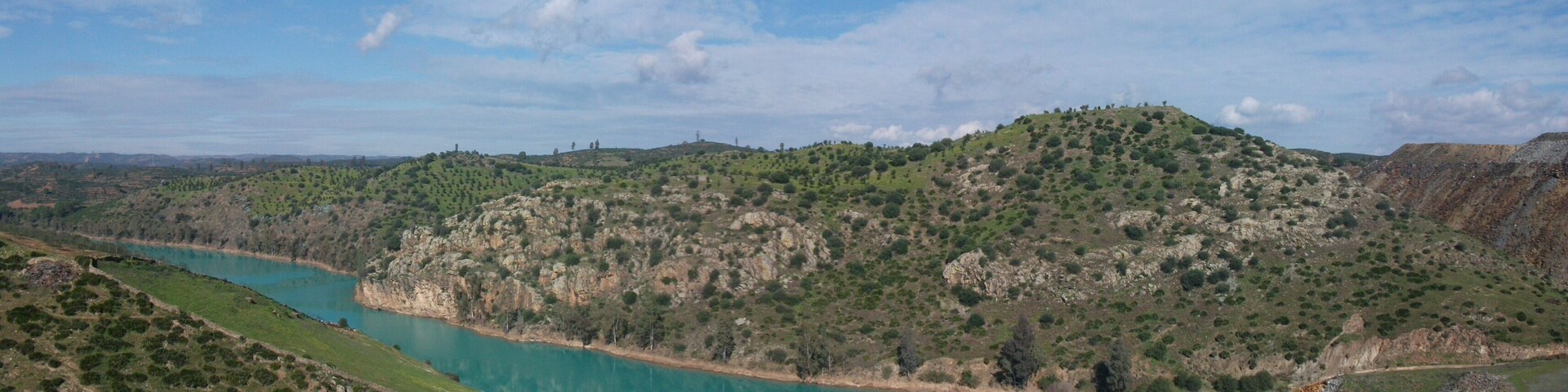 Rio Agrio a la altura del casco municipal de Aznalcóllar que queda a la izquierda de la imagen y fuera de ella. A la derecha están las escombreras de las antiguas minas de pirita. El color turquesa es debido a la contaminación residual que proviene de las escorrentias de las escombreras.
