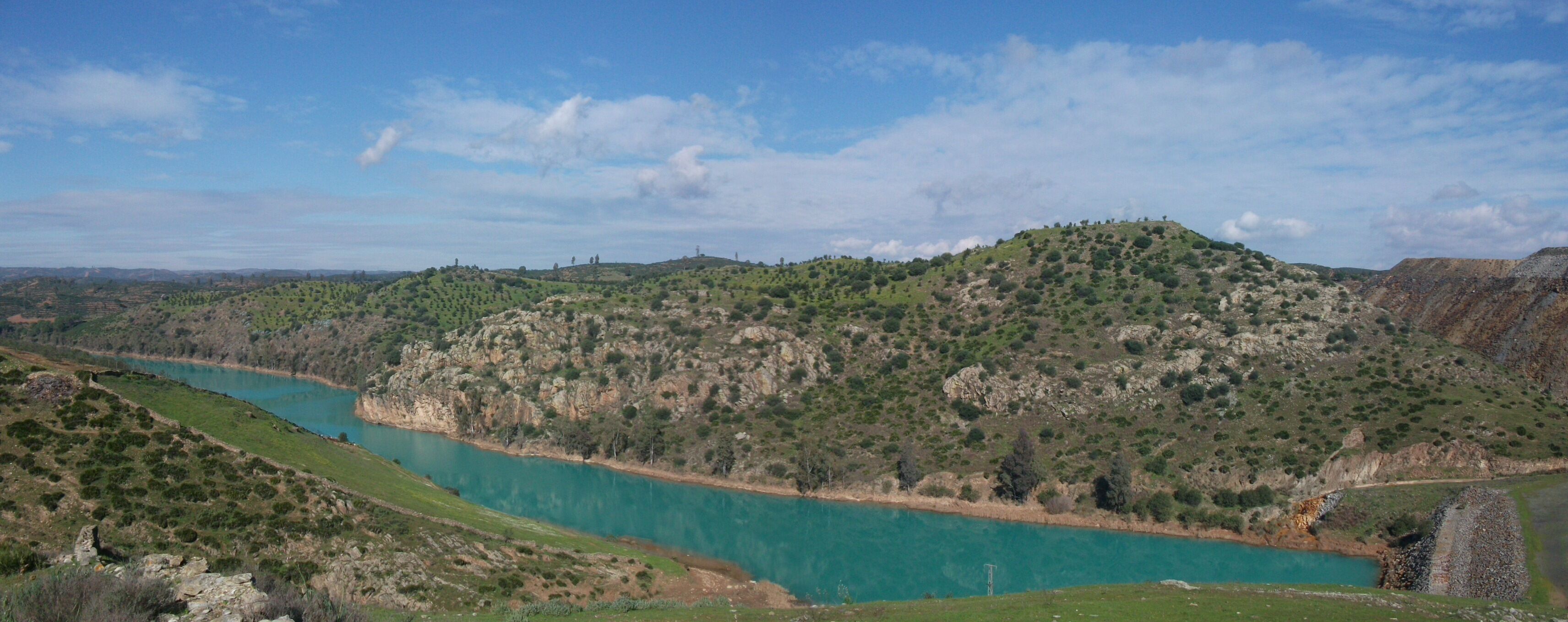 A turquoise river winding through a hilly landscape with sparse vegetation and a clear sky.