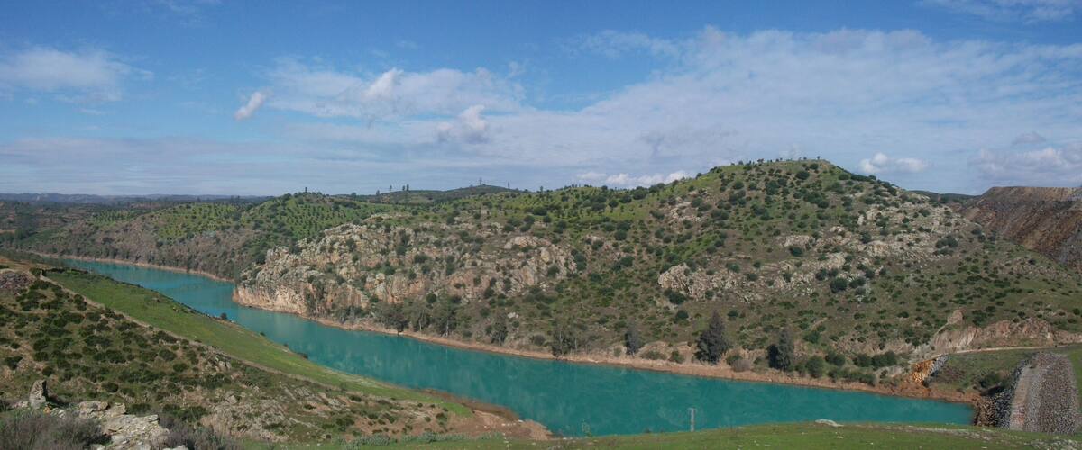 A turquoise river winding through a hilly landscape with sparse vegetation and a clear sky.