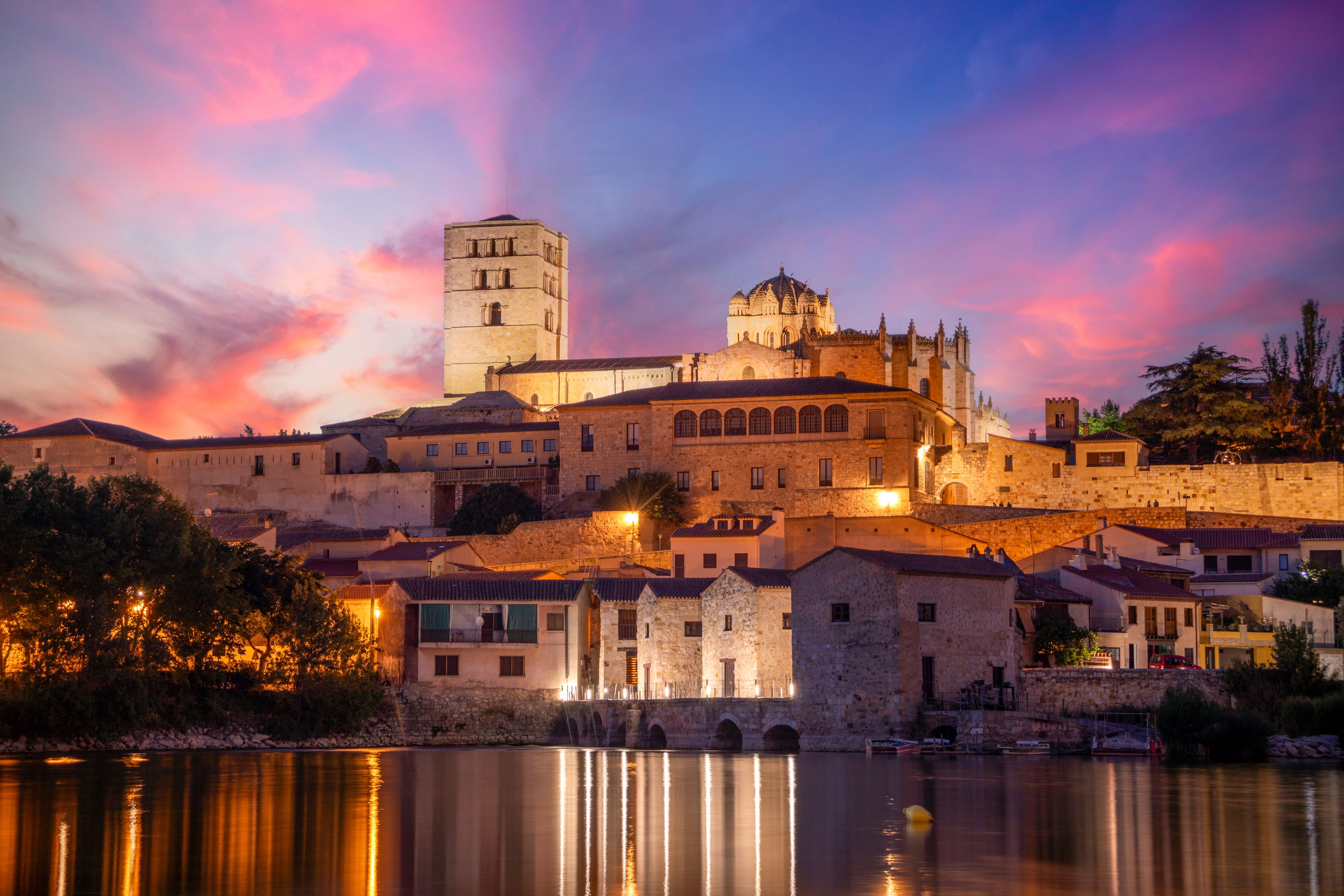 Un paisaje urbano histórico con una torre y una catedral destacadas que se reflejan en el agua.