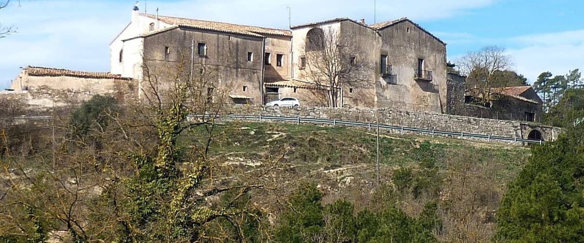 A historic stone building with a tower, surrounded by dense shrubbery and trees.