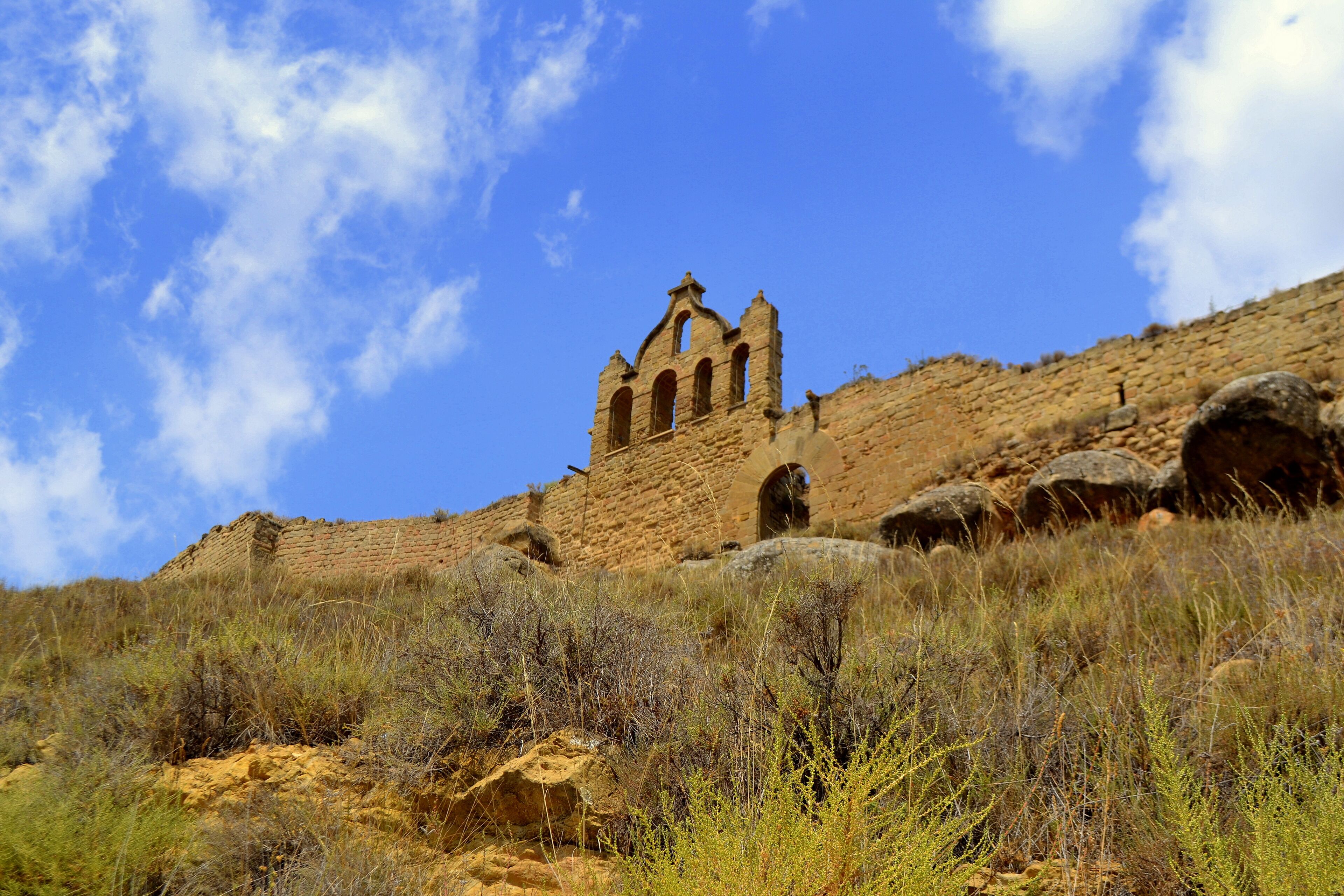 A ruined stone structure with arches on a hillside under a clear blue sky.