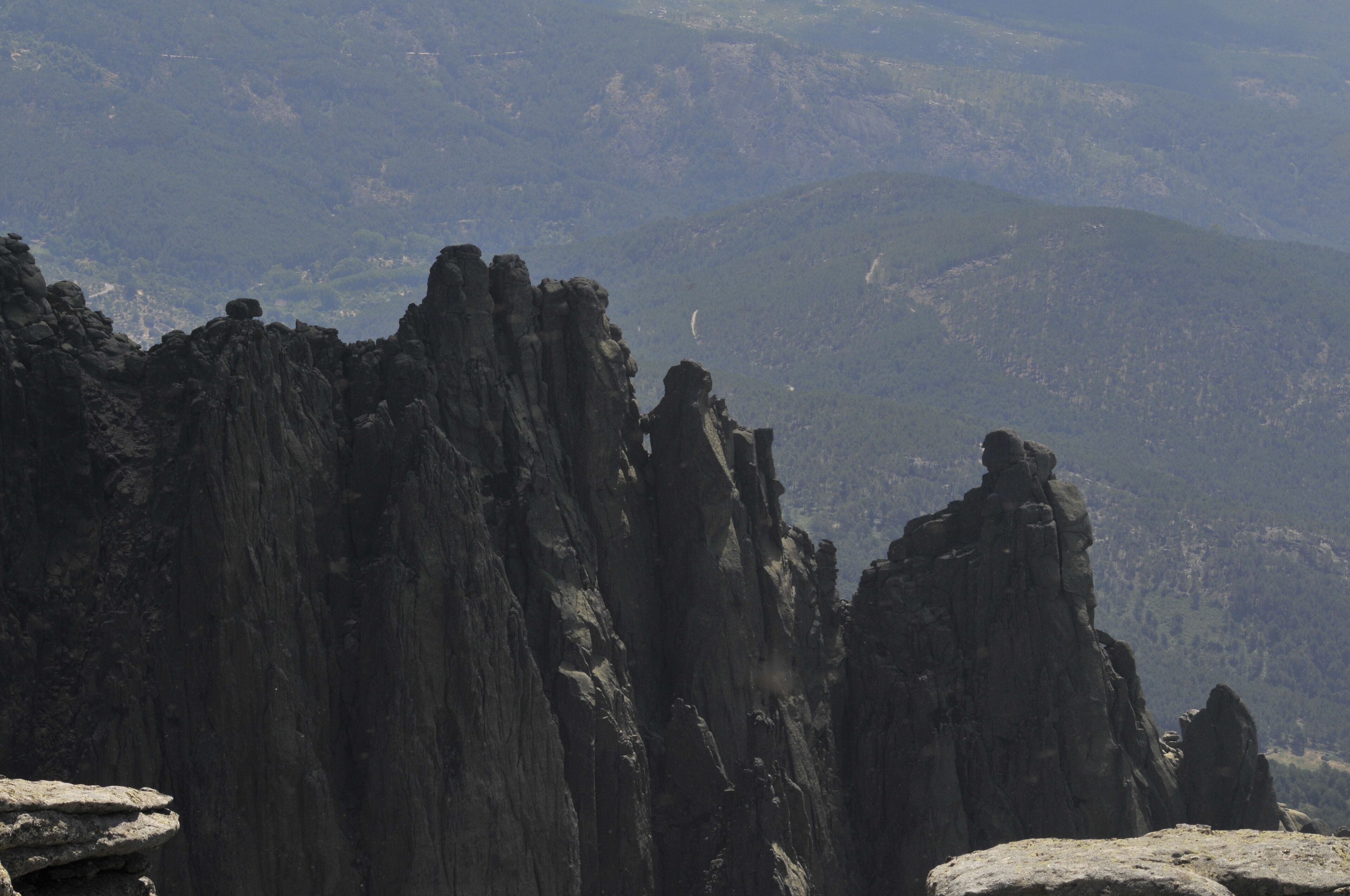 A rugged mountain landscape with prominent rock formations and a distant view of a valley.