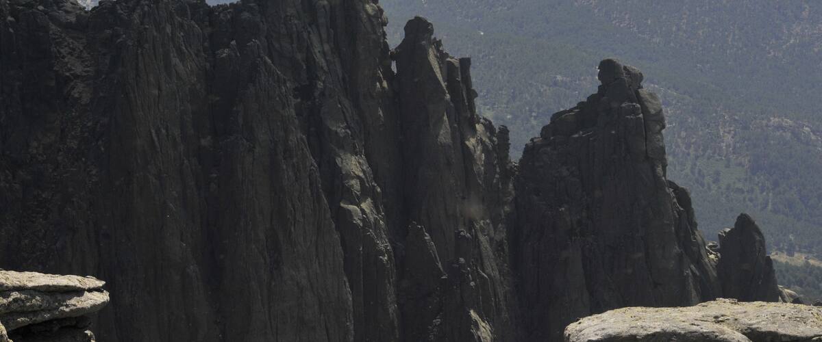 A rugged mountain landscape with prominent rock formations and a distant view of a valley.