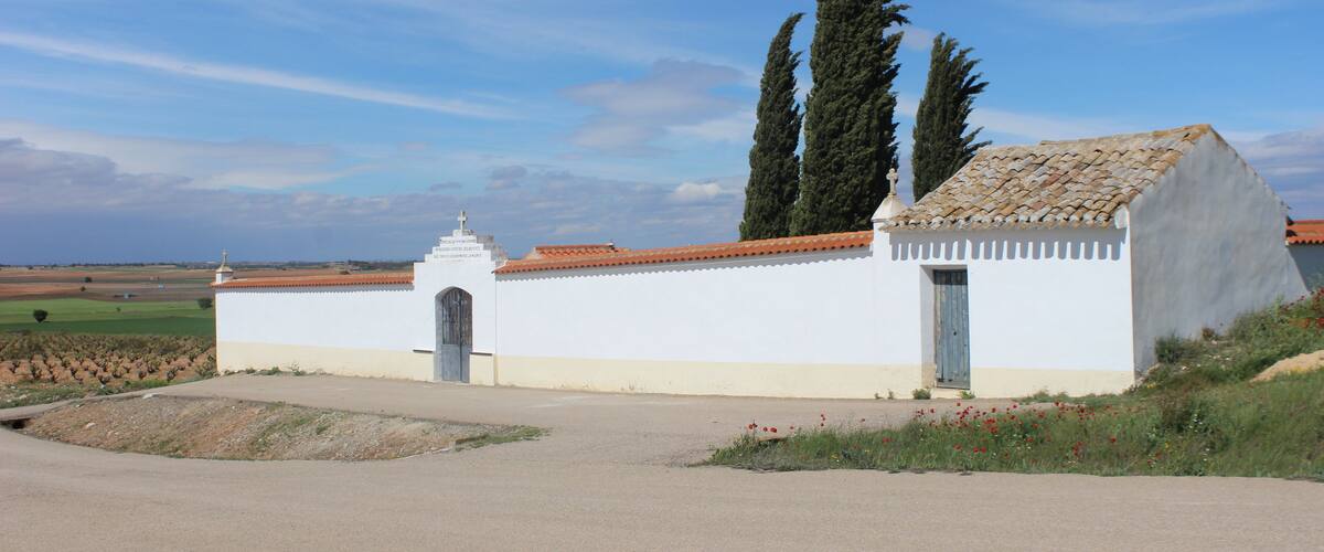 A white church with a tiled roof, surrounded by fields and tall cypress trees.