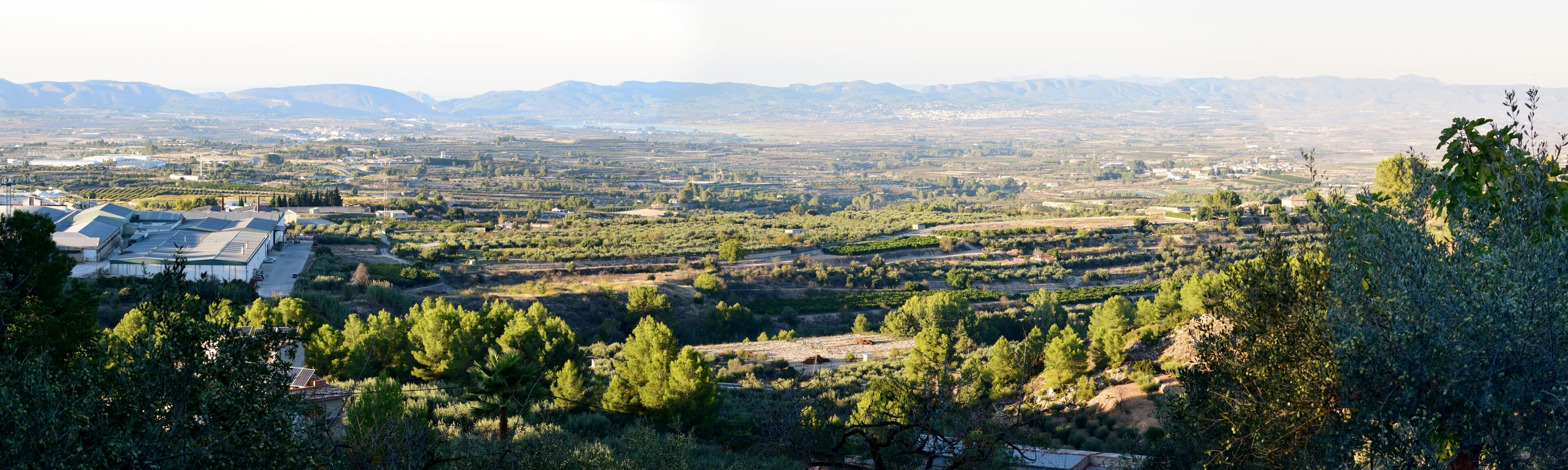 A rural landscape with terraced fields, a few buildings, and distant mountains.