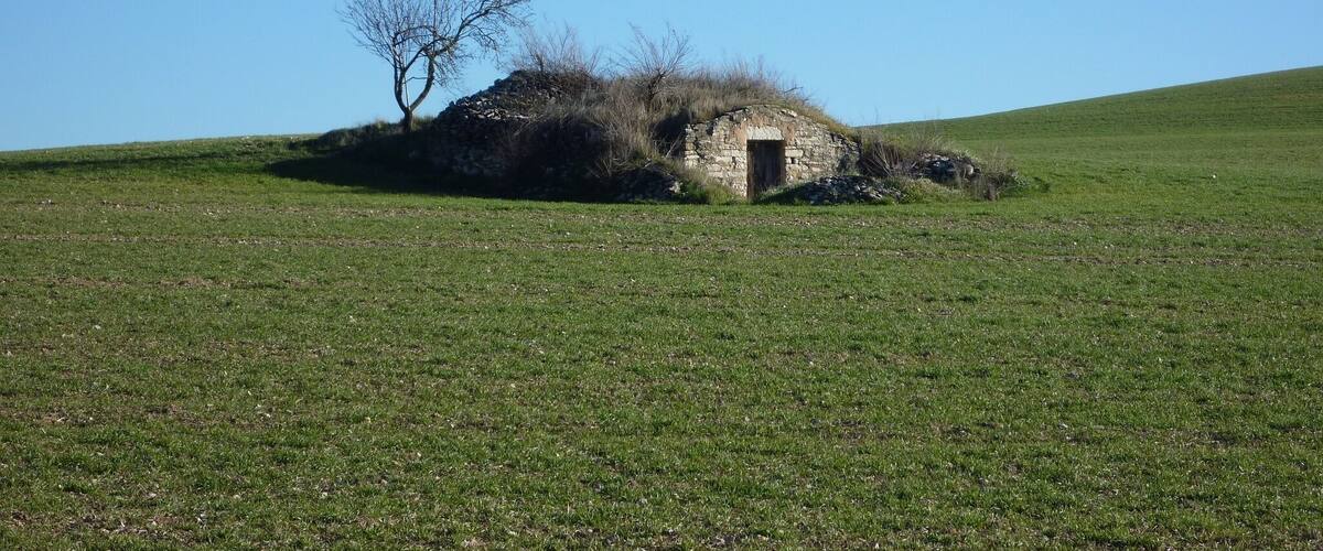 A stone hut on a grassy hill with a clear blue sky.