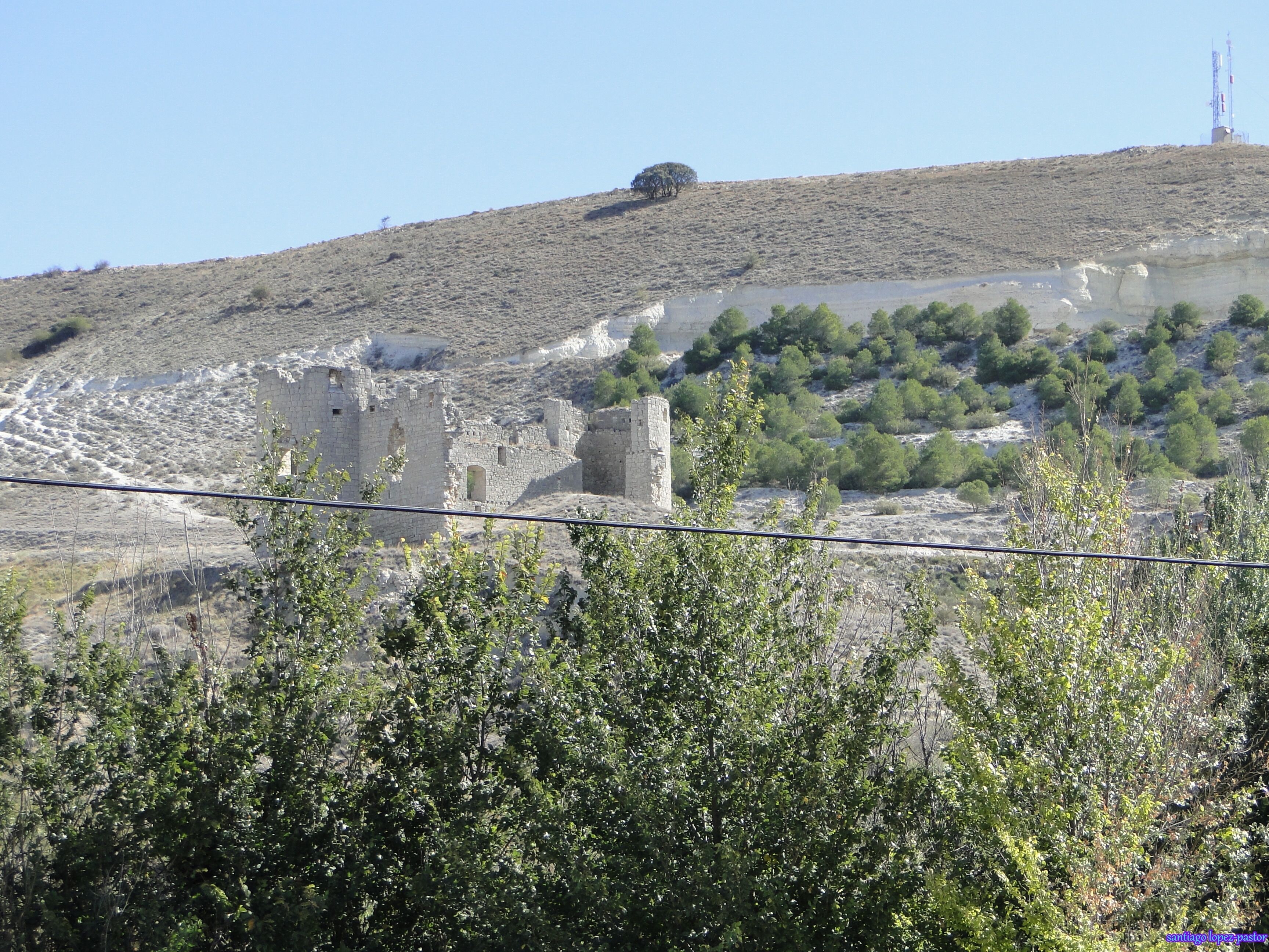 A historical stone structure on a hill with sparse vegetation and a clear sky.