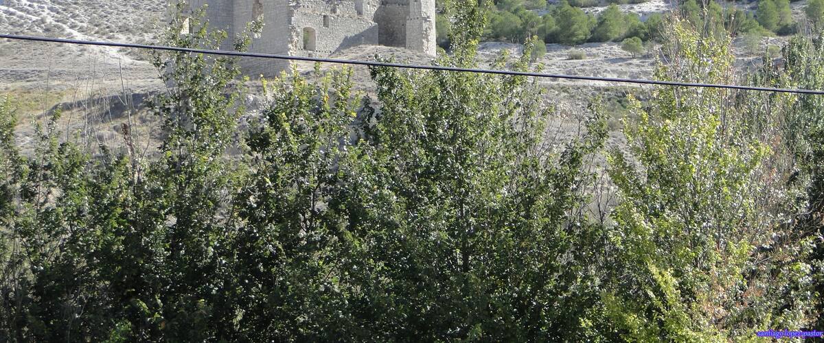 A historical stone structure on a hill with sparse vegetation and a clear sky.